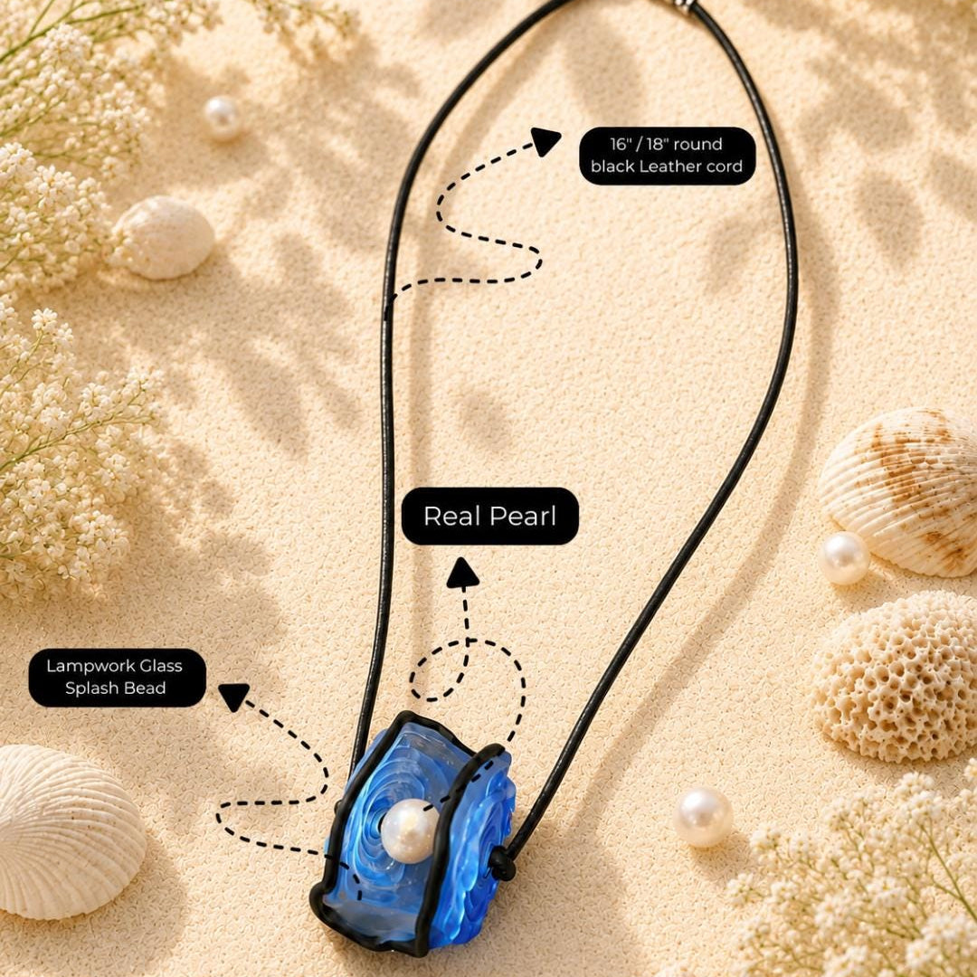 A necklace laid flat on a sandy surface with seashells and dried flowers around it. The product is a black leather cord necklace with a blue translucent lampwork glass pendant and a white faux pearl at the center.