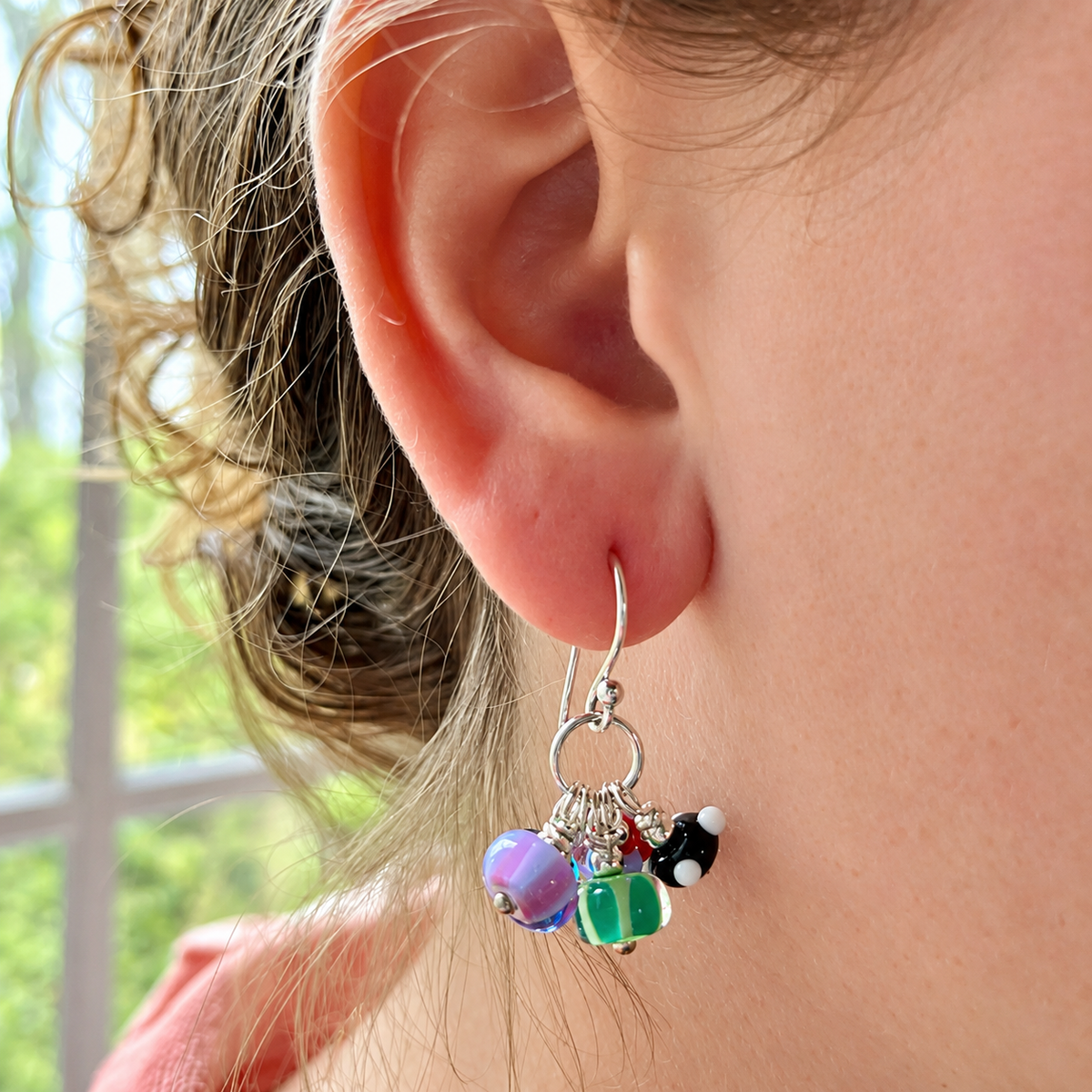A close-up of a person's ear wearing a silver hoop earring with dangling colorful beads, including purple, green, black, and white.
