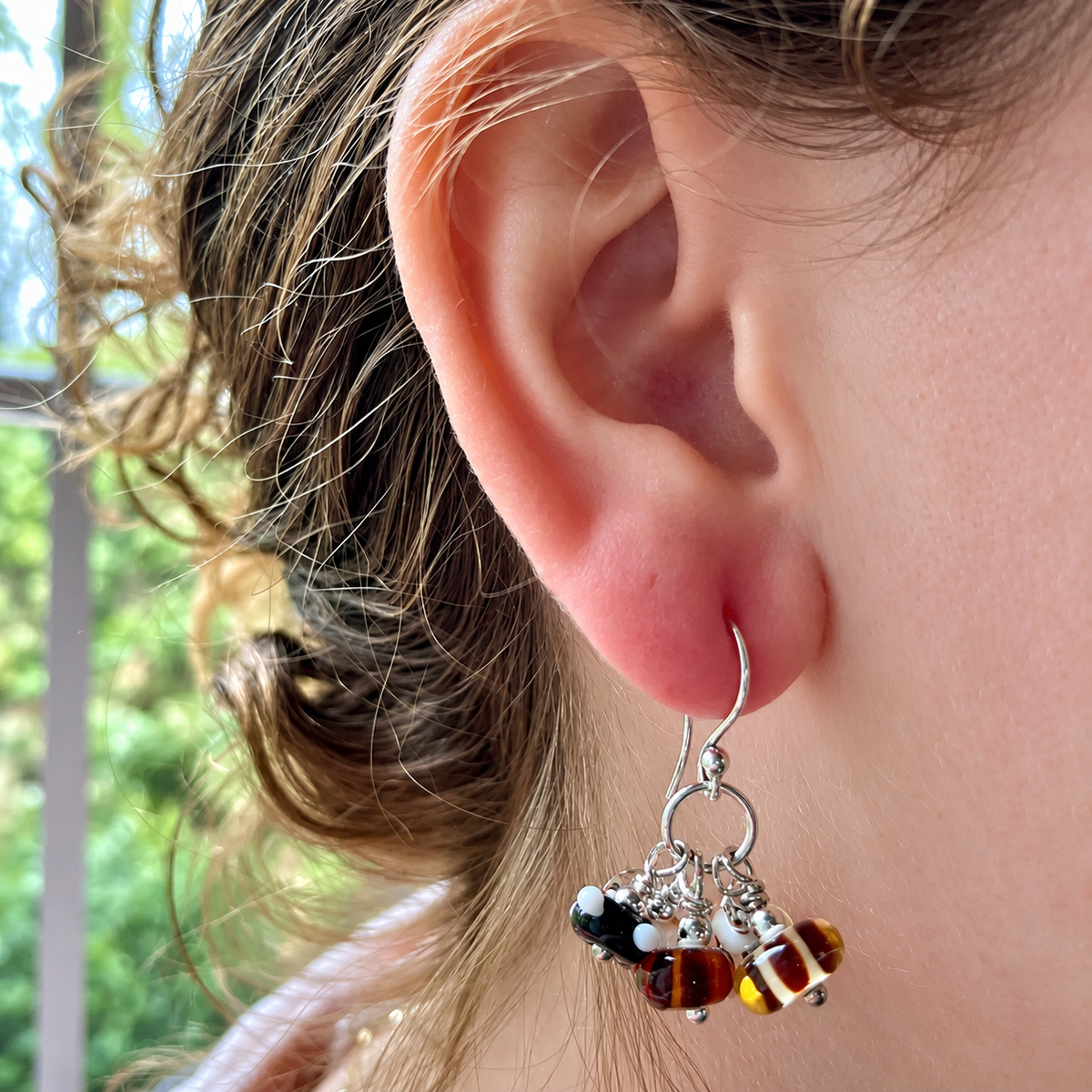 A close-up of a person's ear wearing a silver-toned dangle earring with small beads and amber-colored glass beads.