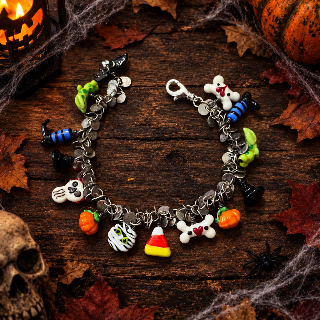 A silver charm bracelet with Halloween-themed charms, including a skull, mummy, candy corn, bones, and small boots, displayed on a rustic wooden surface.