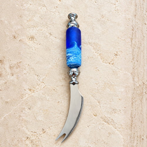 A curved metal cheese knife with a decorative blue and white marbled glass handle, displayed on a light beige stone surface.