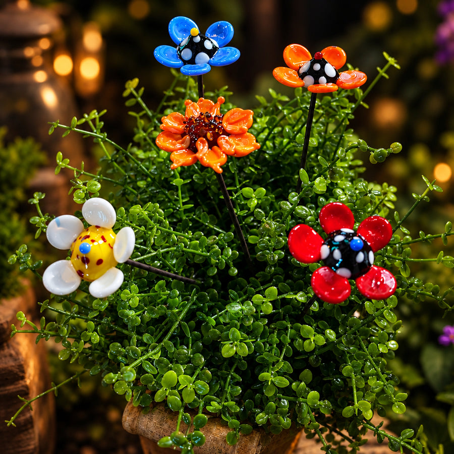 A glass flower bundle featuring five colorful flower-shaped plant stakes styled in a lush green succulent arrangement. The flowers include blue, orange, white, red, and yellow designs with black and white polka dot centers.