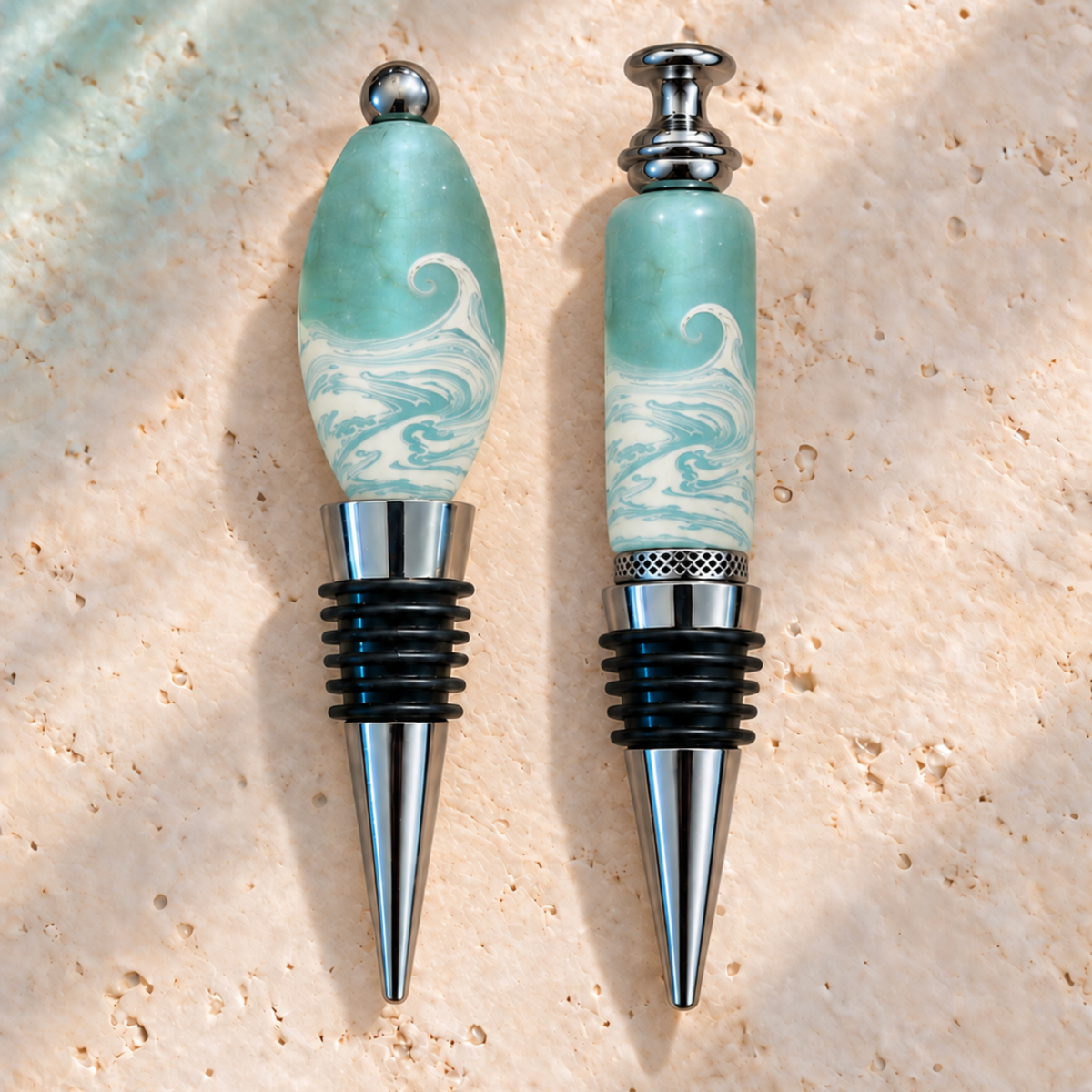 Two wine bottle stoppers with light blue and white marbled wave-patterned handles and silver metal bases, displayed on a textured beige stone surface.